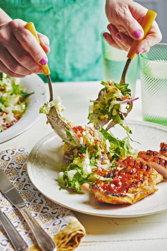 Woman putting Late Summer Cobb Salad on a plate with chicken.