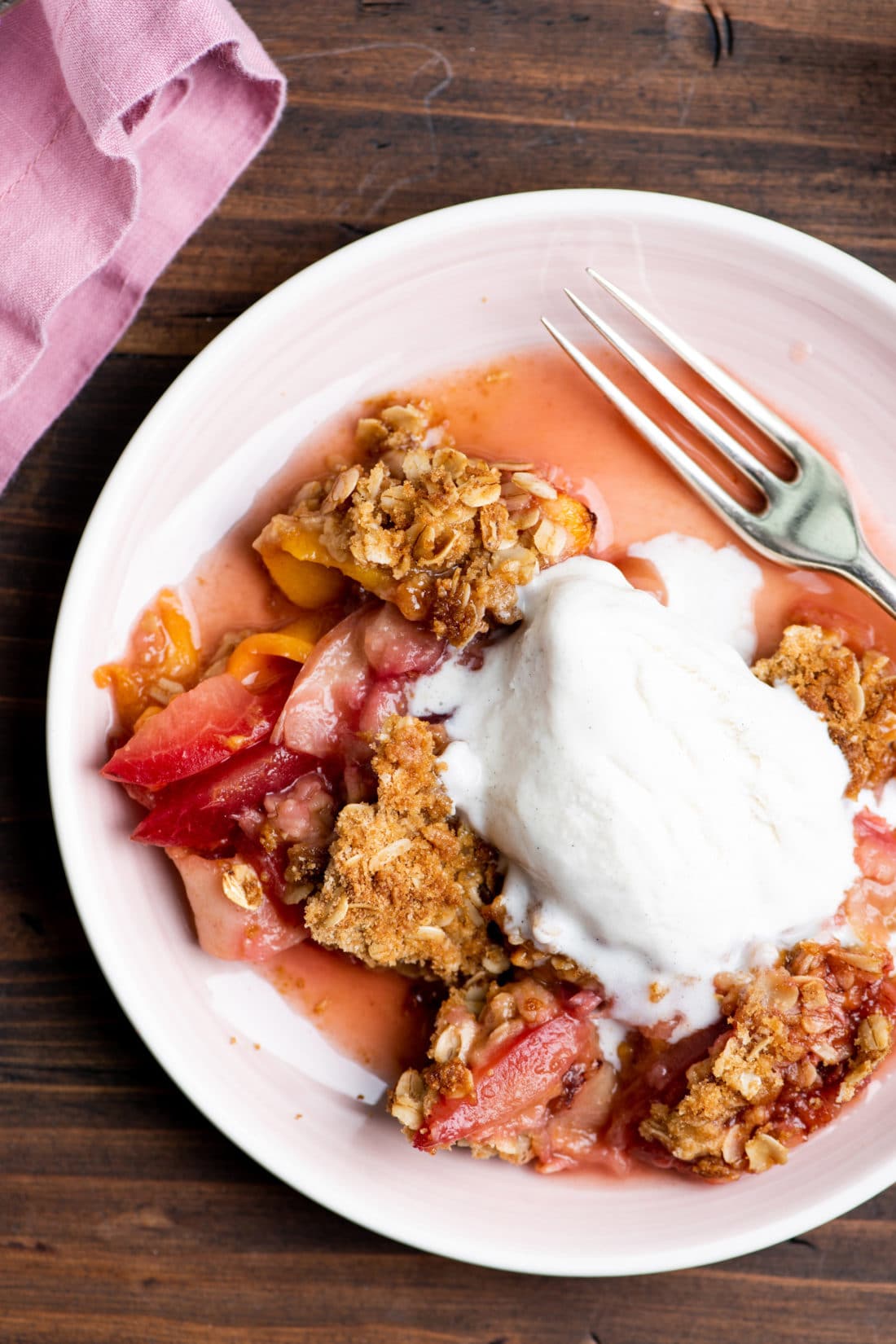 Fork on a plate of Plum and Nectarine Crisp topped with ice cream.