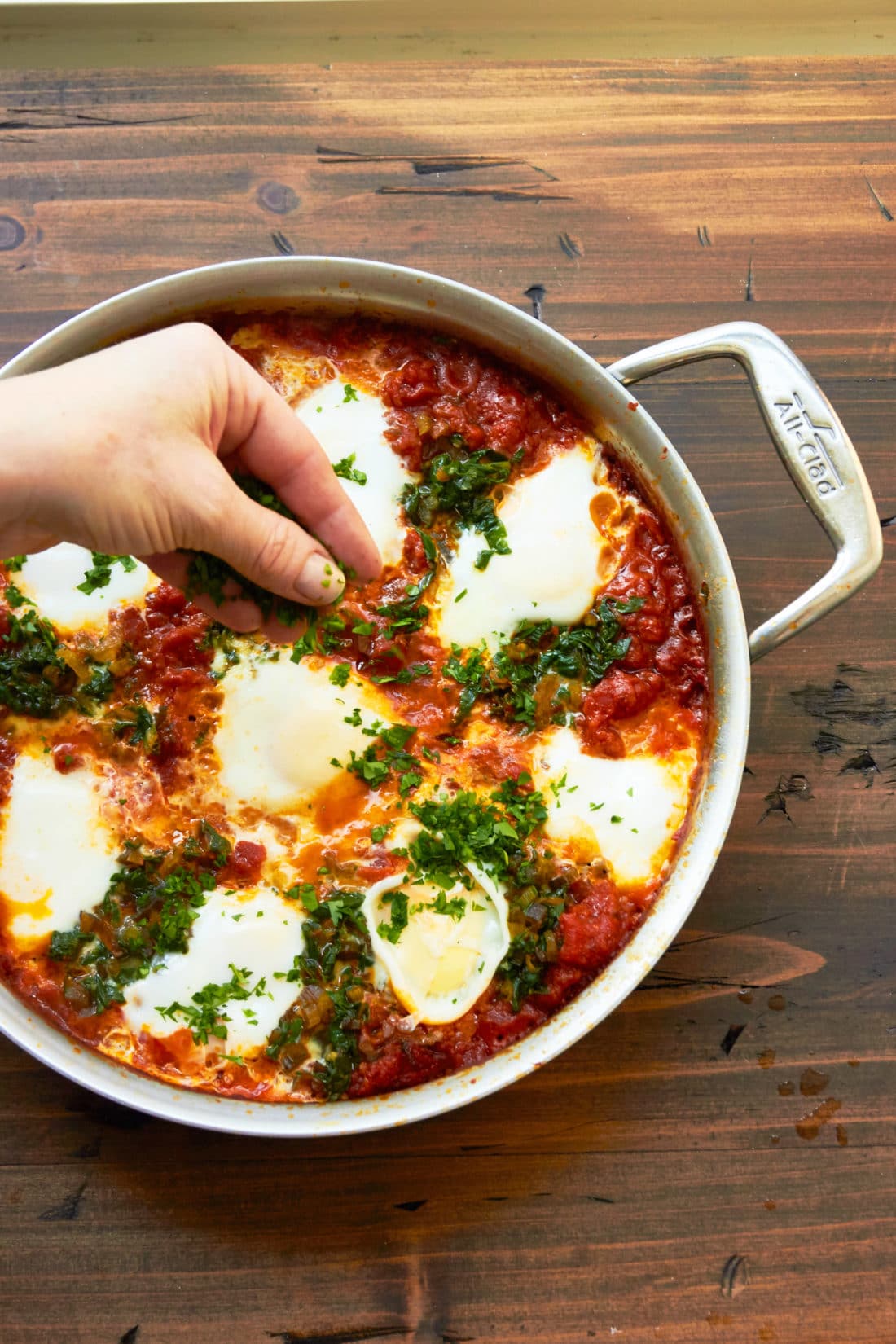 Adding parsley to Shakshuka with Swiss Chard in pan.