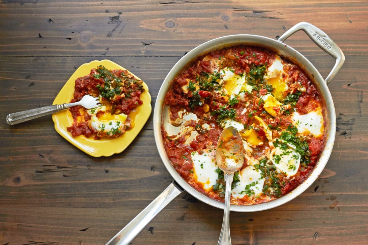 Shakshuka with Swiss Chard in frying pan and on yellow plate.