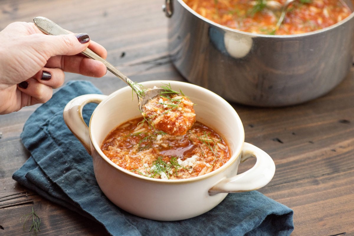 Spoon scooping Tomato, Orzo and Dill Soup from a bowl.