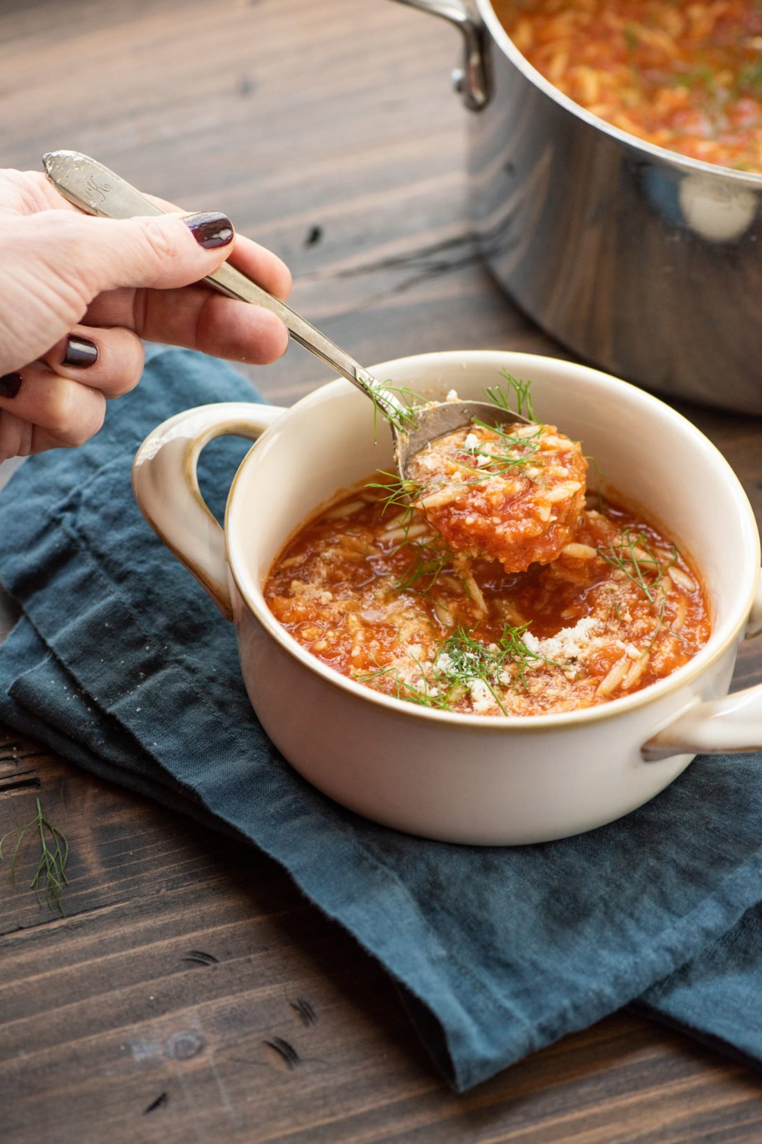 Woman scooping Tomato, Orzo and Dill Soup with a spoon.