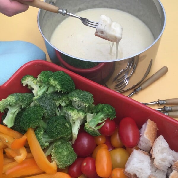 Fork dipping bread into Classic Swiss Fondue next to a tray of veggies.
