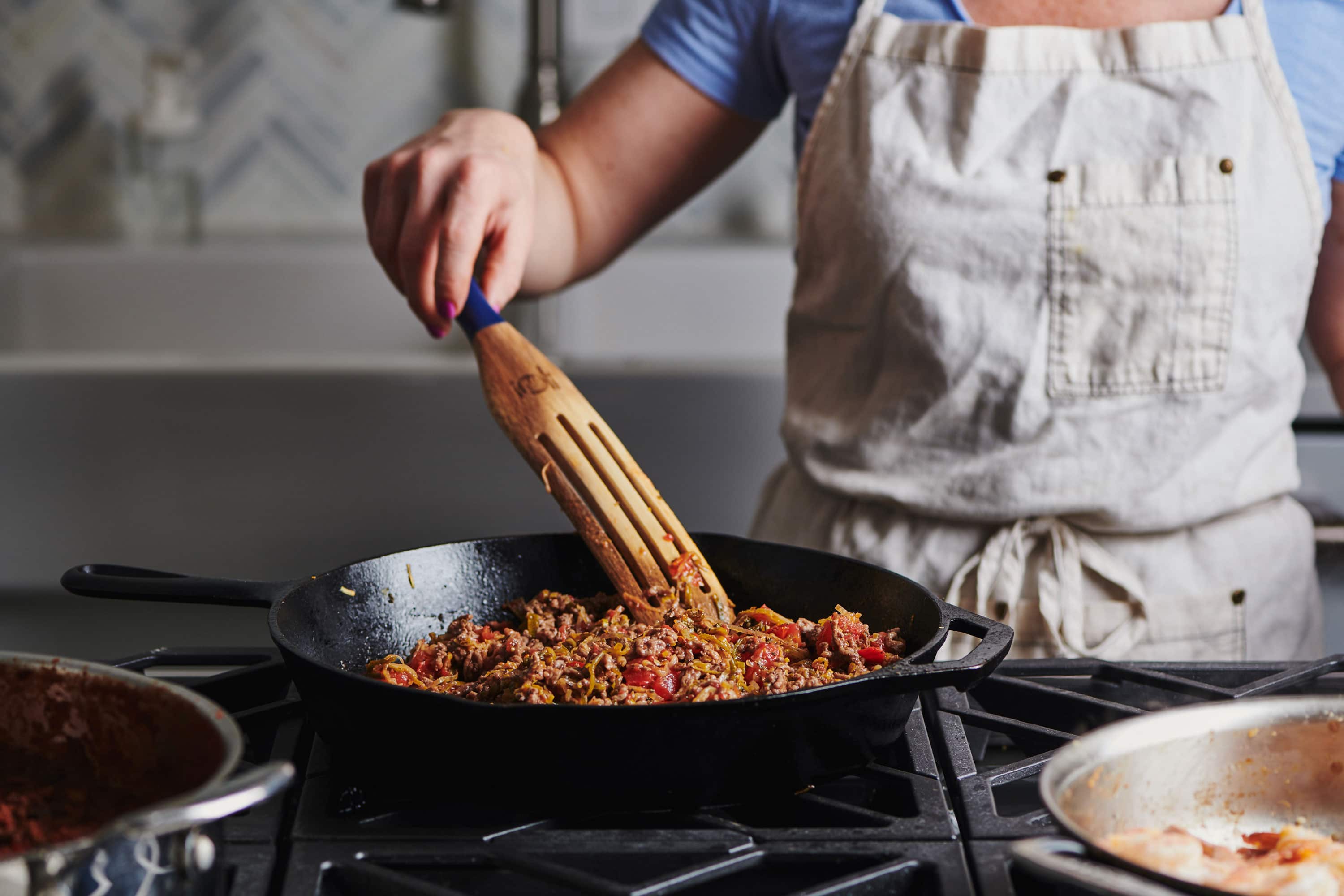 Woman stirring Ground Beef Chili with a wooden spatula.