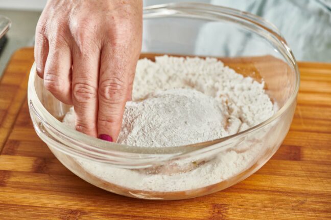 Woman dredging chicken in flour.