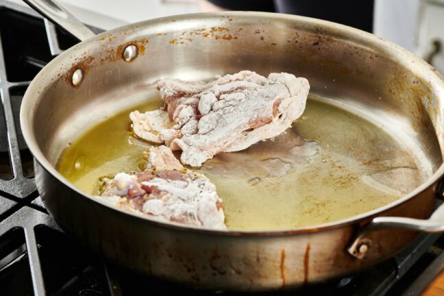 Floured chicken in a skillet.
