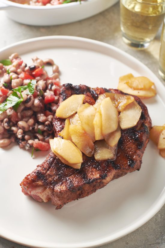 Plate of Pork Chops topped with Apples next to a Black Eyed Pea Salad.