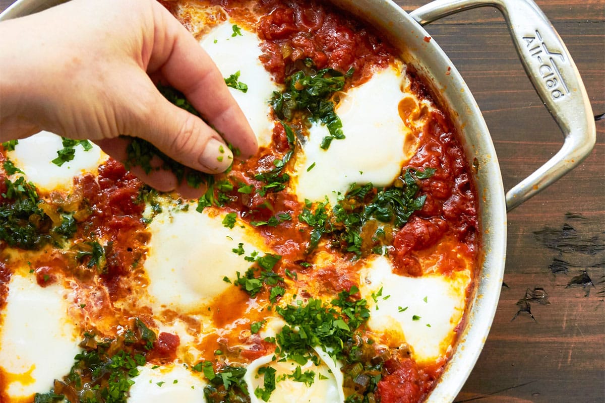 Adding parsley to Shakshuka with Swiss Chard in pan.