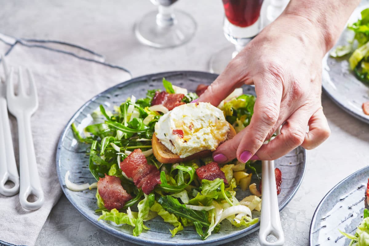 Woman placing bread topped with warm goat cheese on a Bistro Salad.