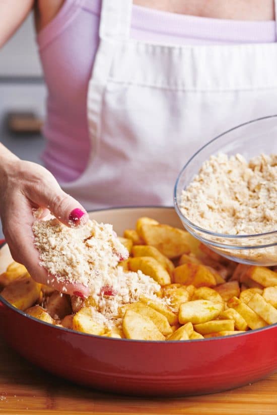 Woman adding streusel topping to apple crisp