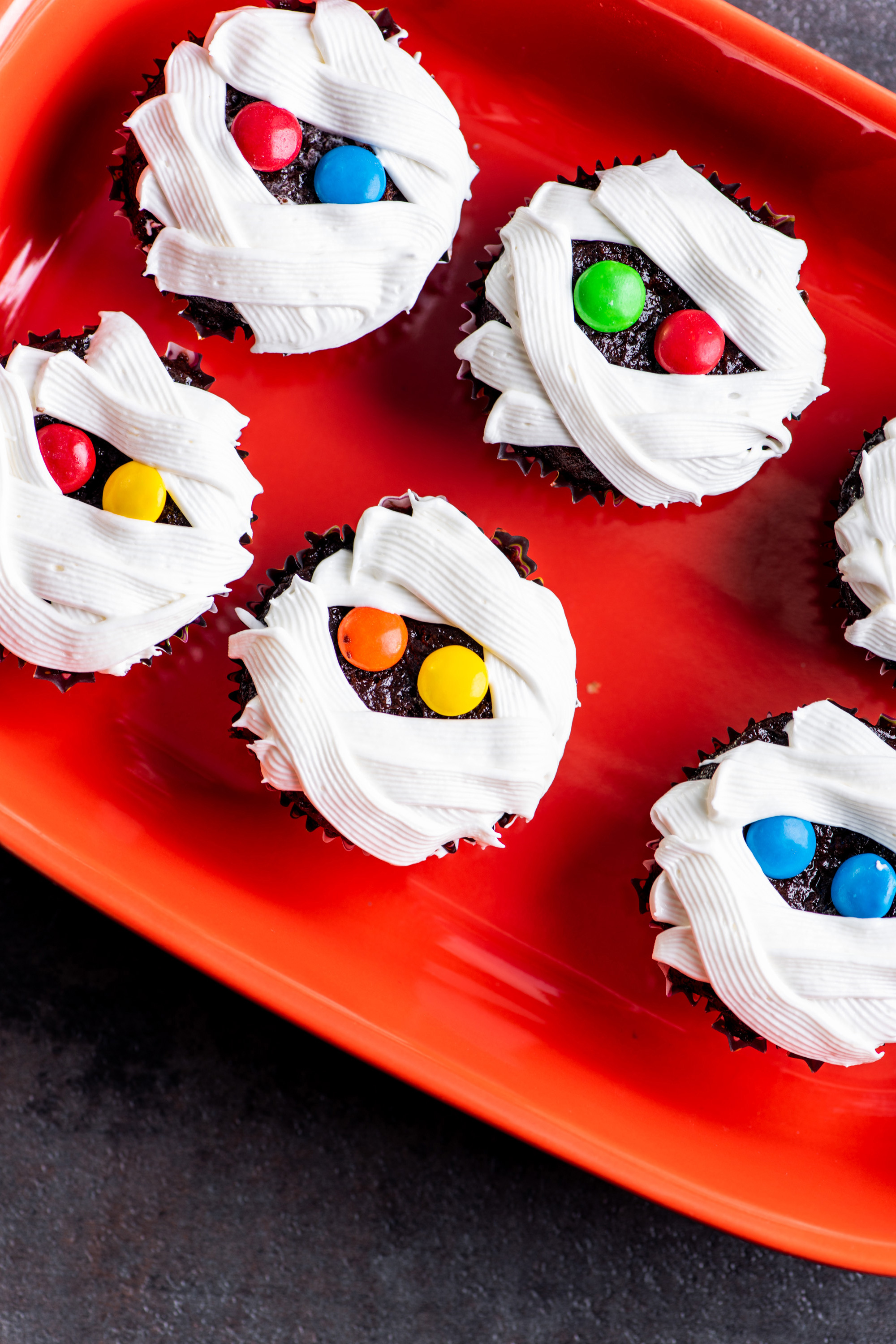 Cupcakes with white frosting and candies decorated to look like mummies.