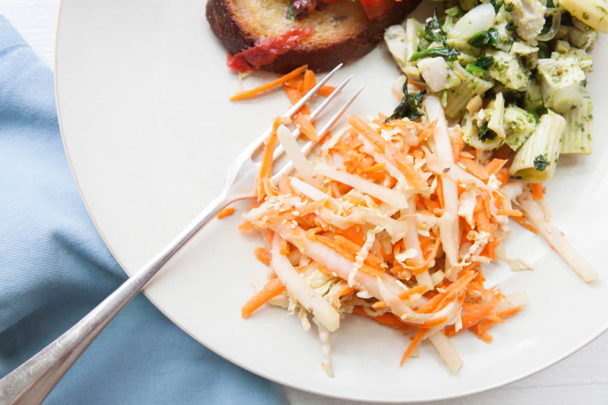 Carrot, Cabbage and Kohlrabi Slaw on plate with other dishes.