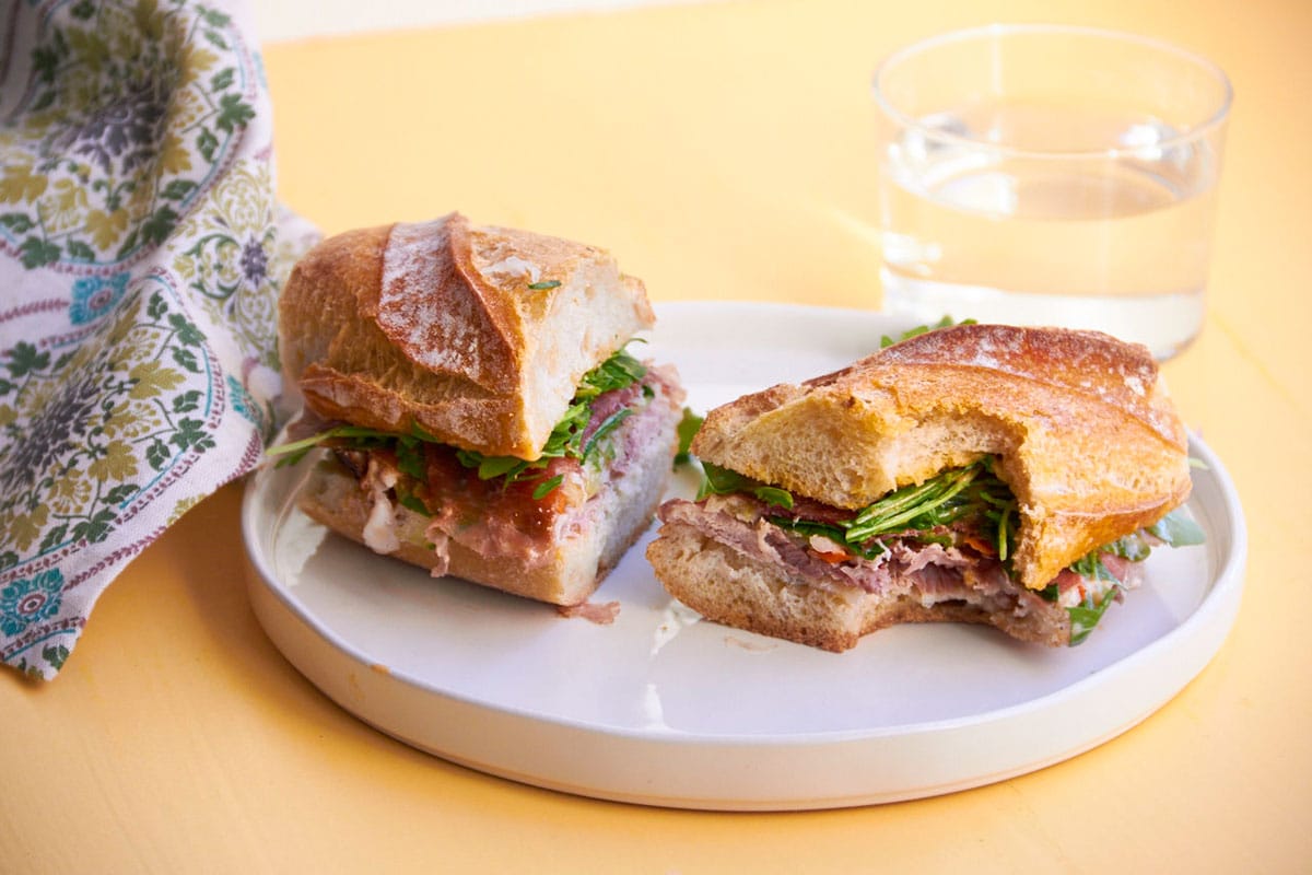 White plate with Prosciutto and Pork Banh Mi on yellow table.