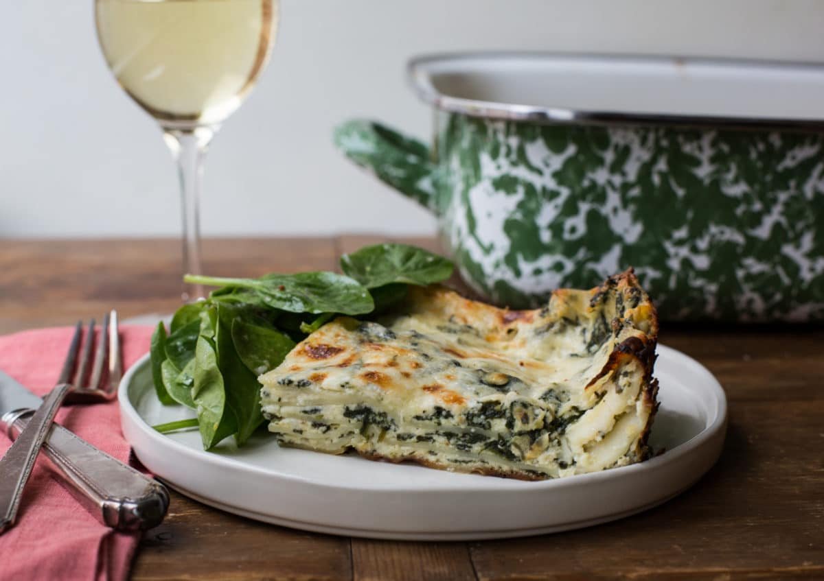 Slice of Cheesy White and Green Spinach Lasagna on plate with wine glass.