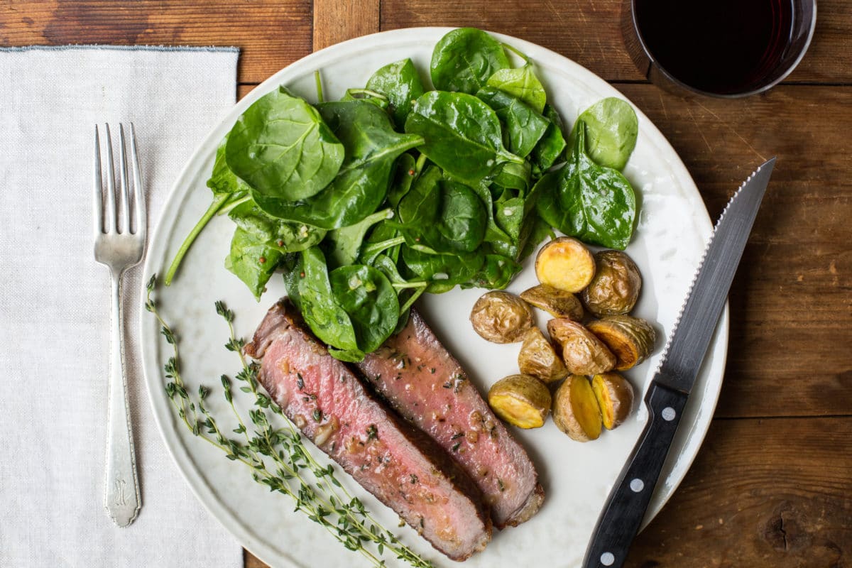 Plate with ribeye in thyme-garlic butter, salad, and roasted potatoes.