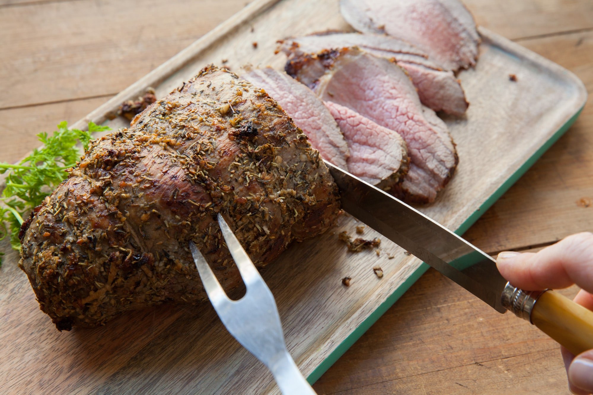 Roast Eye of Round Beef with Thyme and Rosemary being sliced on a cutting board.