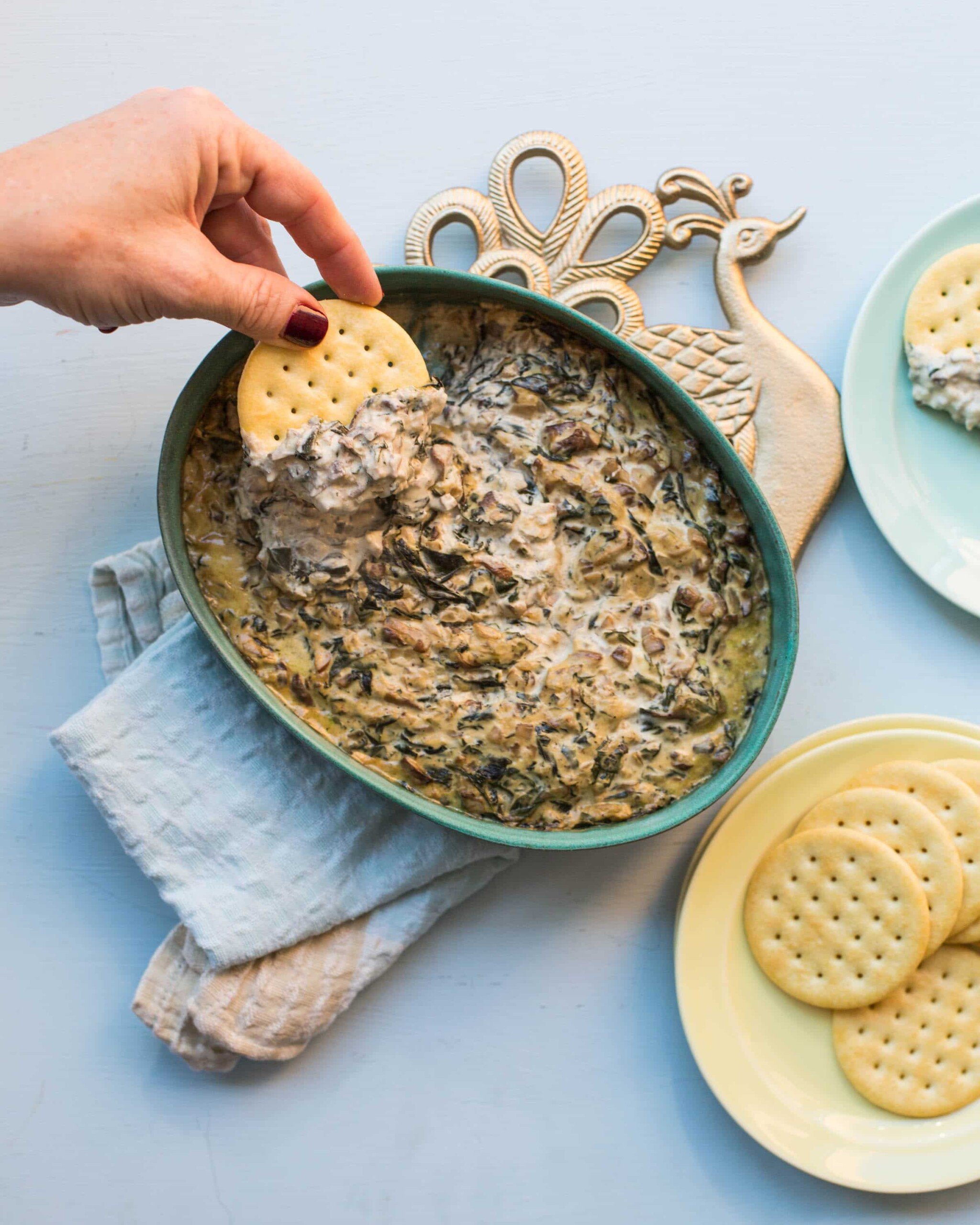 Woman dipping a cracker into Hot Creamy Mushroom and Spinach Dip.