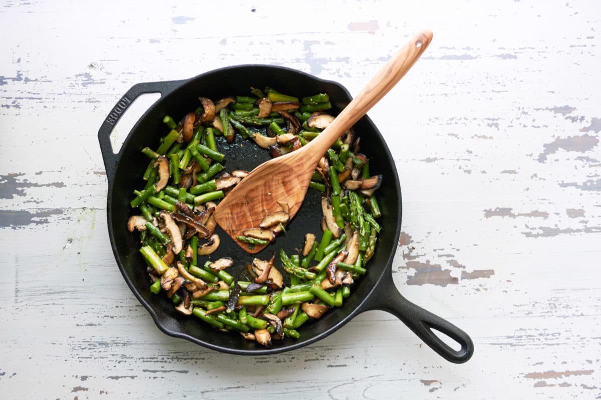 Sesame Asparagus and Shiitake Mushrooms in a skillet with a wooden spatula.