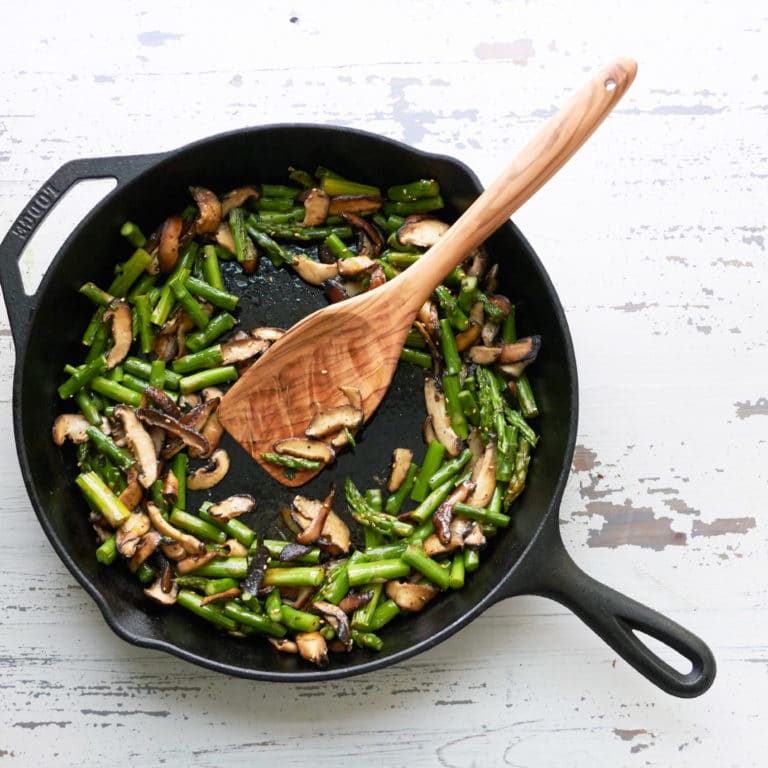 Sesame Asparagus and Shiitake Mushrooms in a skillet with a wooden spatula.