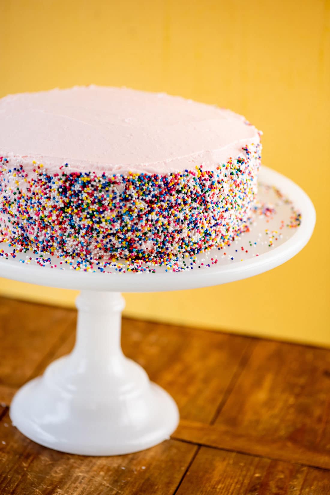 Vanilla Layer Cake with sprinkles on an elevated cake stand.