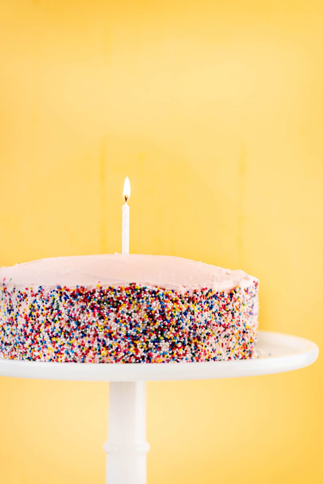 Lit candle in a Vanilla Layer Cake with sprinkles.