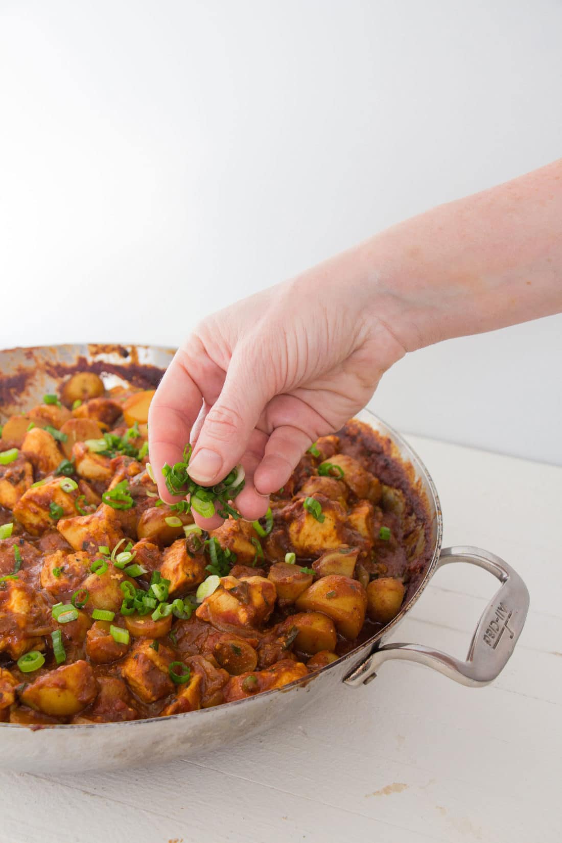 Person sprinkling parsley over Indian Spiced Chicken and Potato Stew.