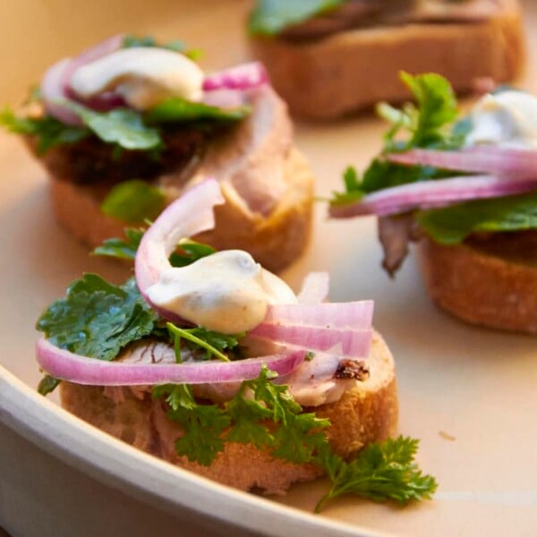 Lamb Crostini with Spiced Crème Fraiche and Herbs on tan plate.