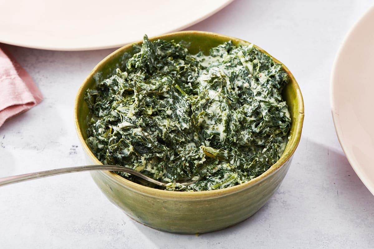 Creamed kale in green bowl with spoon on table.