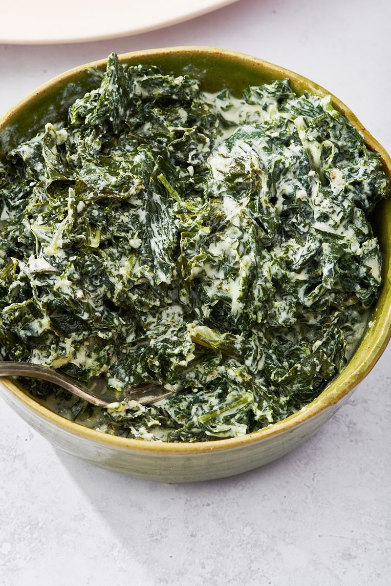 Green bowl of Creamed Kale with a fork.