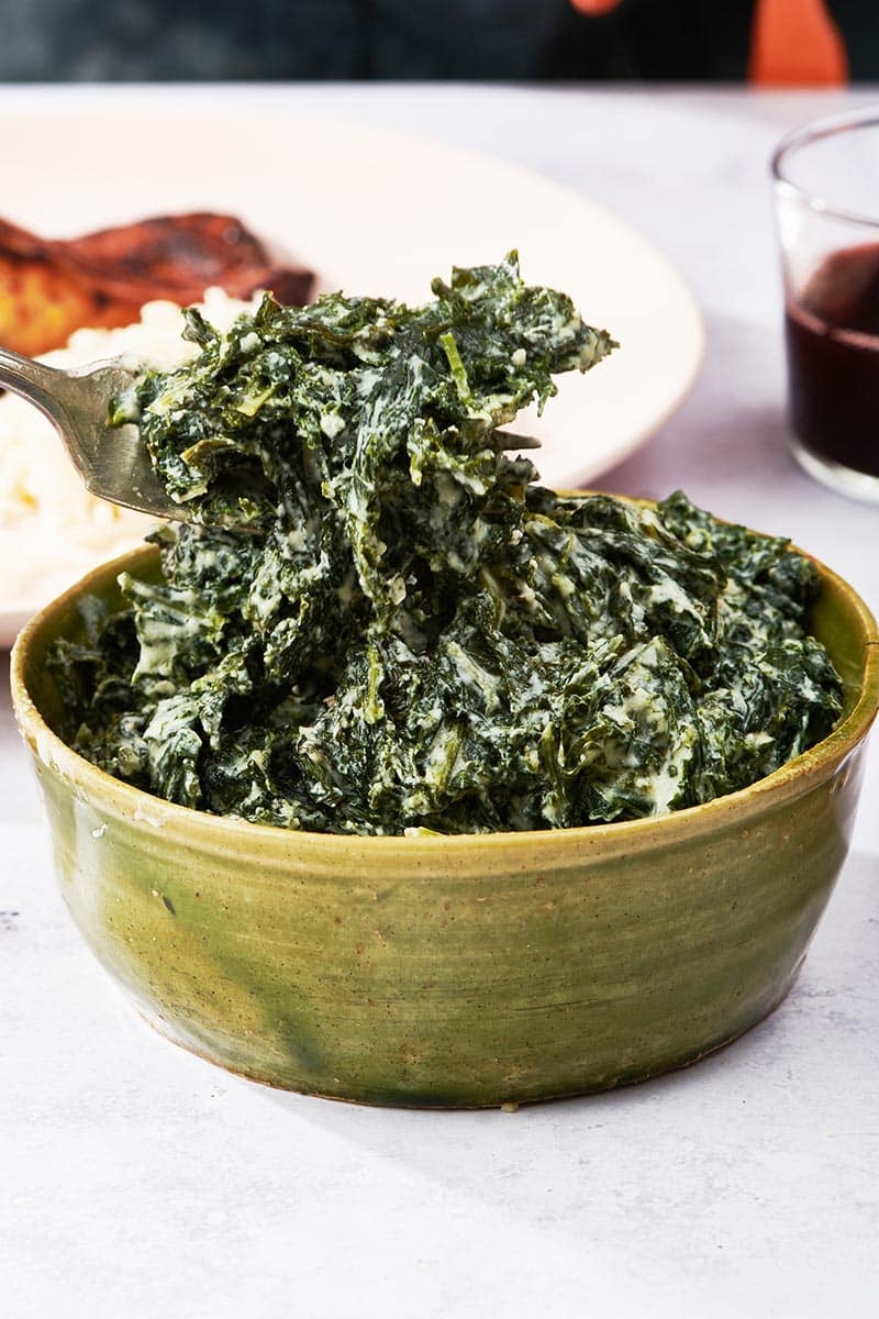Fork grabbing Creamed Kale from a green bowl.