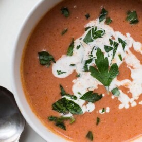 Creamy tomato soup in bowl with spoon on plate.