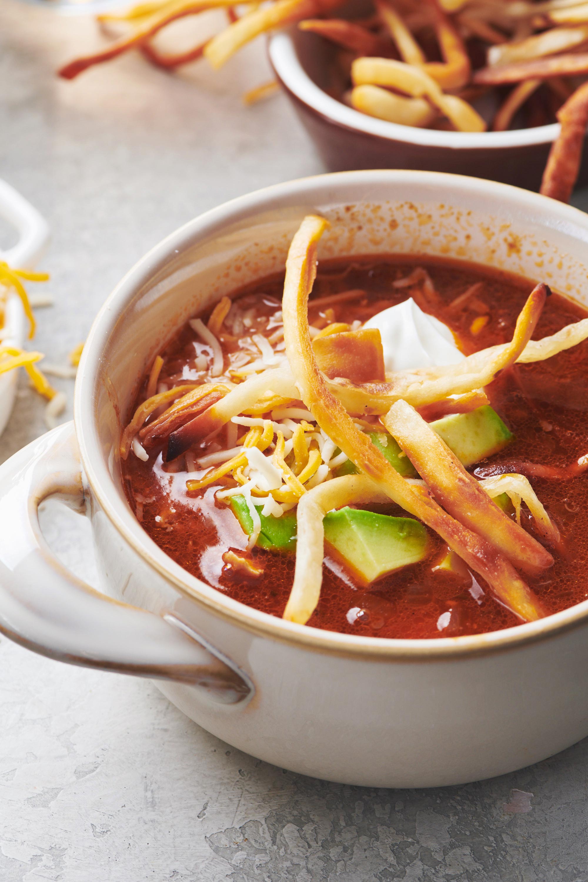 Bowl of Mexican Chicken Tortilla Soup topped with avocado, cheese, and fried tortilla strips.