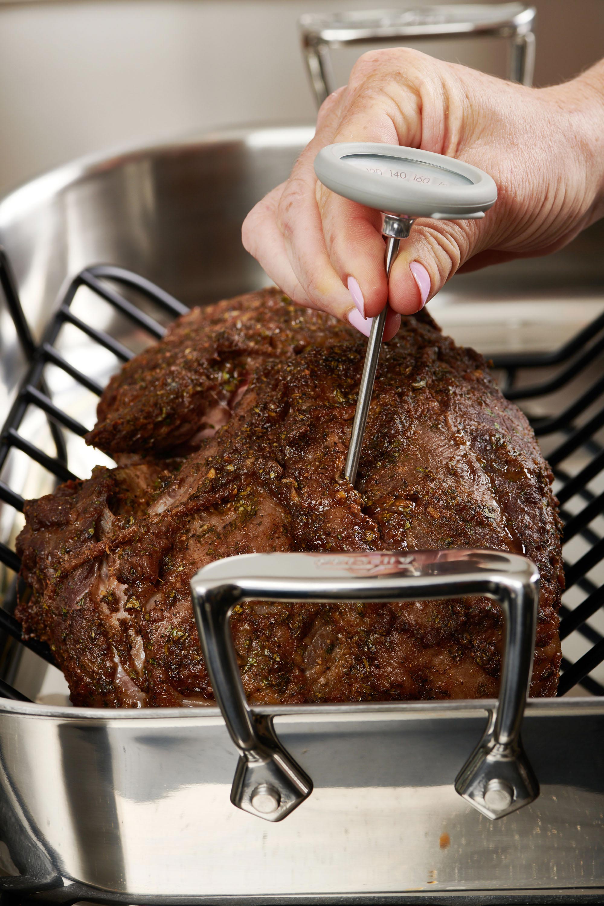 Woman using a thermometer to measure the temperature of Moroccan Leg of Lamb.