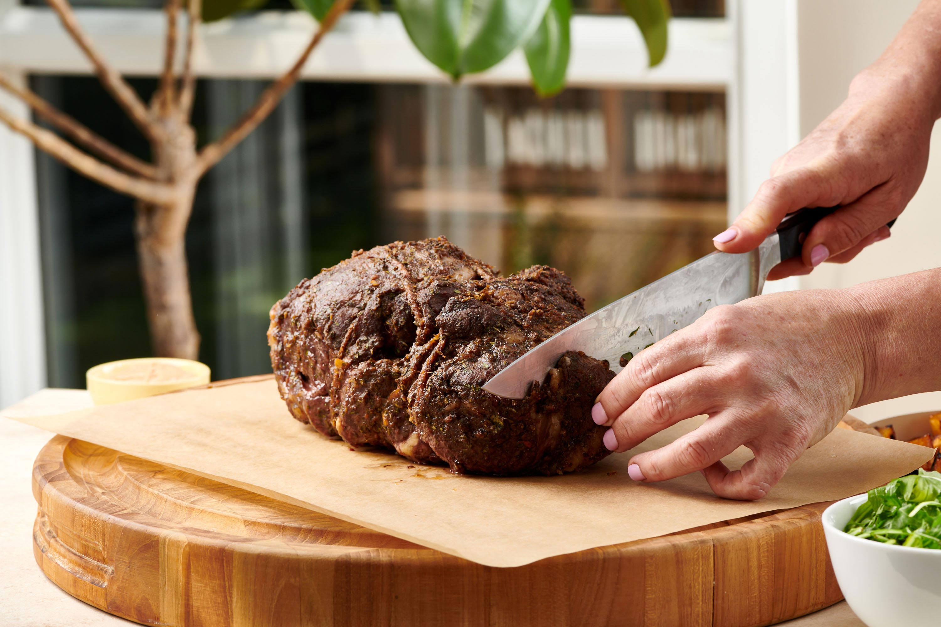 Slicing Slow Cooked Moroccan Leg of Lamb on cutting board with large knife.