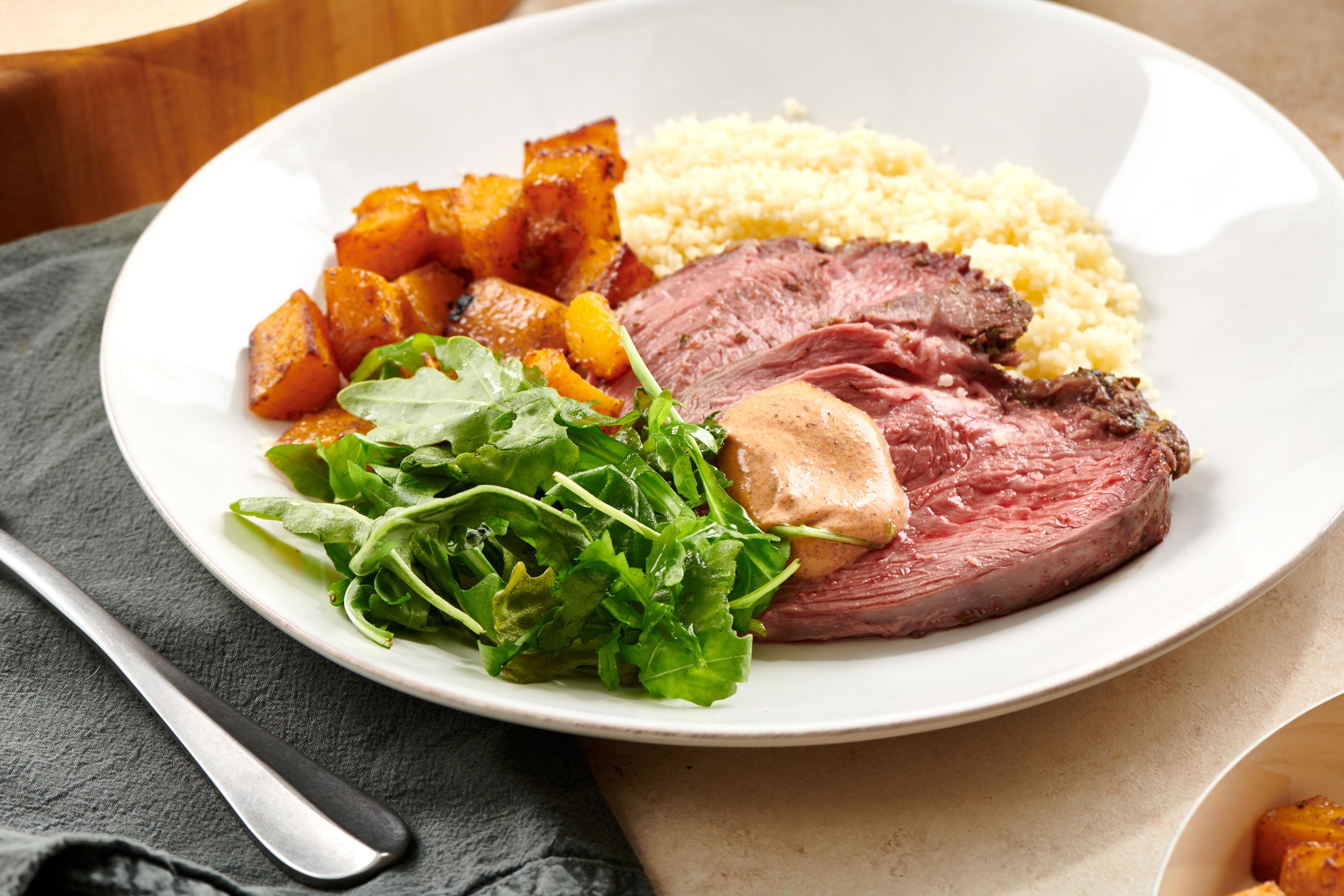 Couscous, arugula, squash, and Moroccan Leg of Lamb with harissa sauce on a plate.