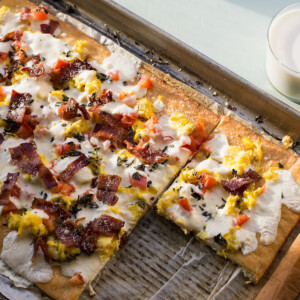 Partially-sliced breakfast pizza on a lined baking sheet.