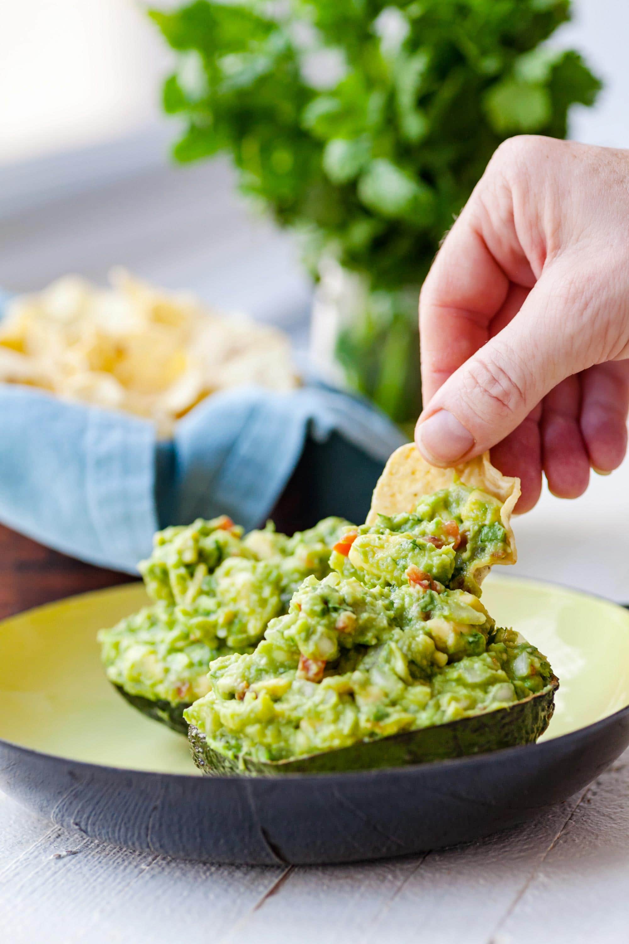 Woman dipping tortilla chip into guacamole.