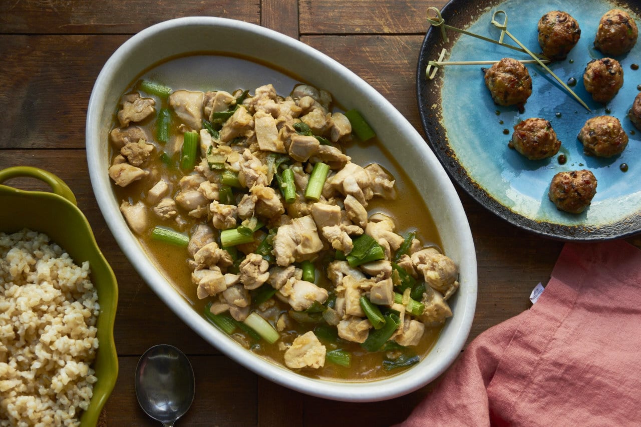 Table set with bowl of chicken stir-fry and Japanese meatballs.
