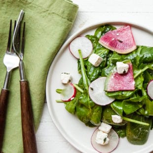 White plate of spinach and radish salad with feta.