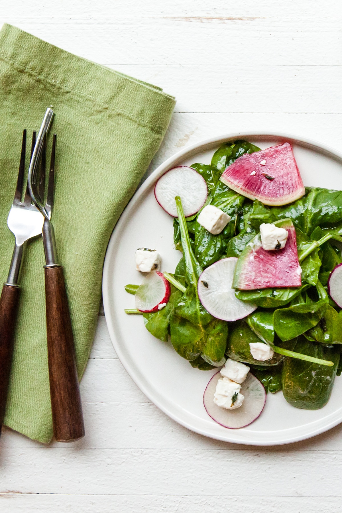 White plate of spinach and radish salad with feta.