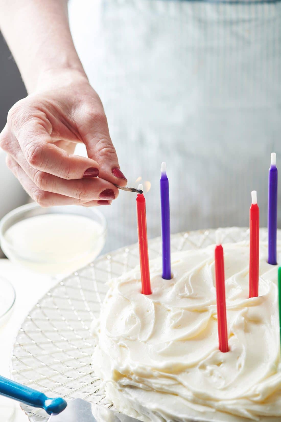 Woman lighting red and blue candles on a Banana Cake with Cream Cheese Frosting.