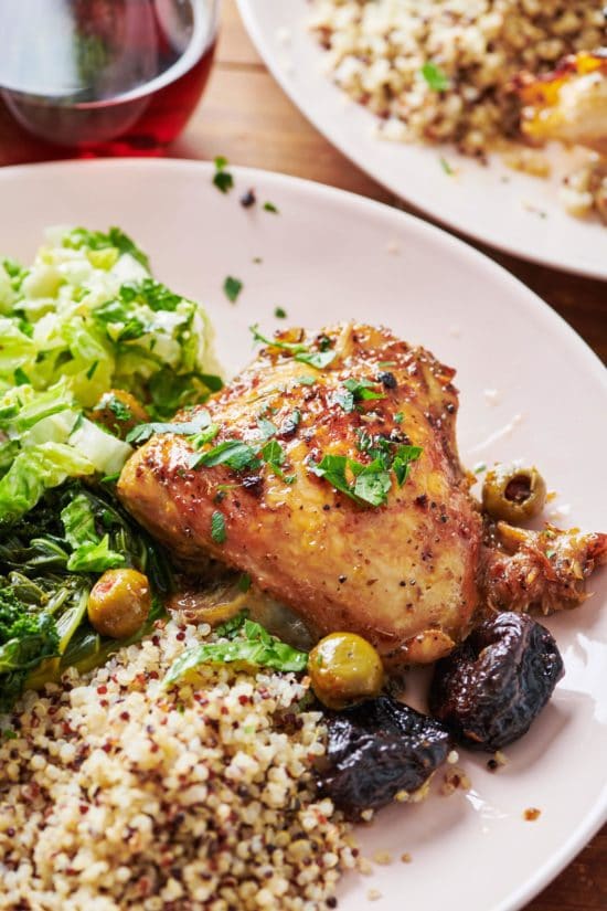 Chicken Marbella on a plate with olives, salad, and grains.