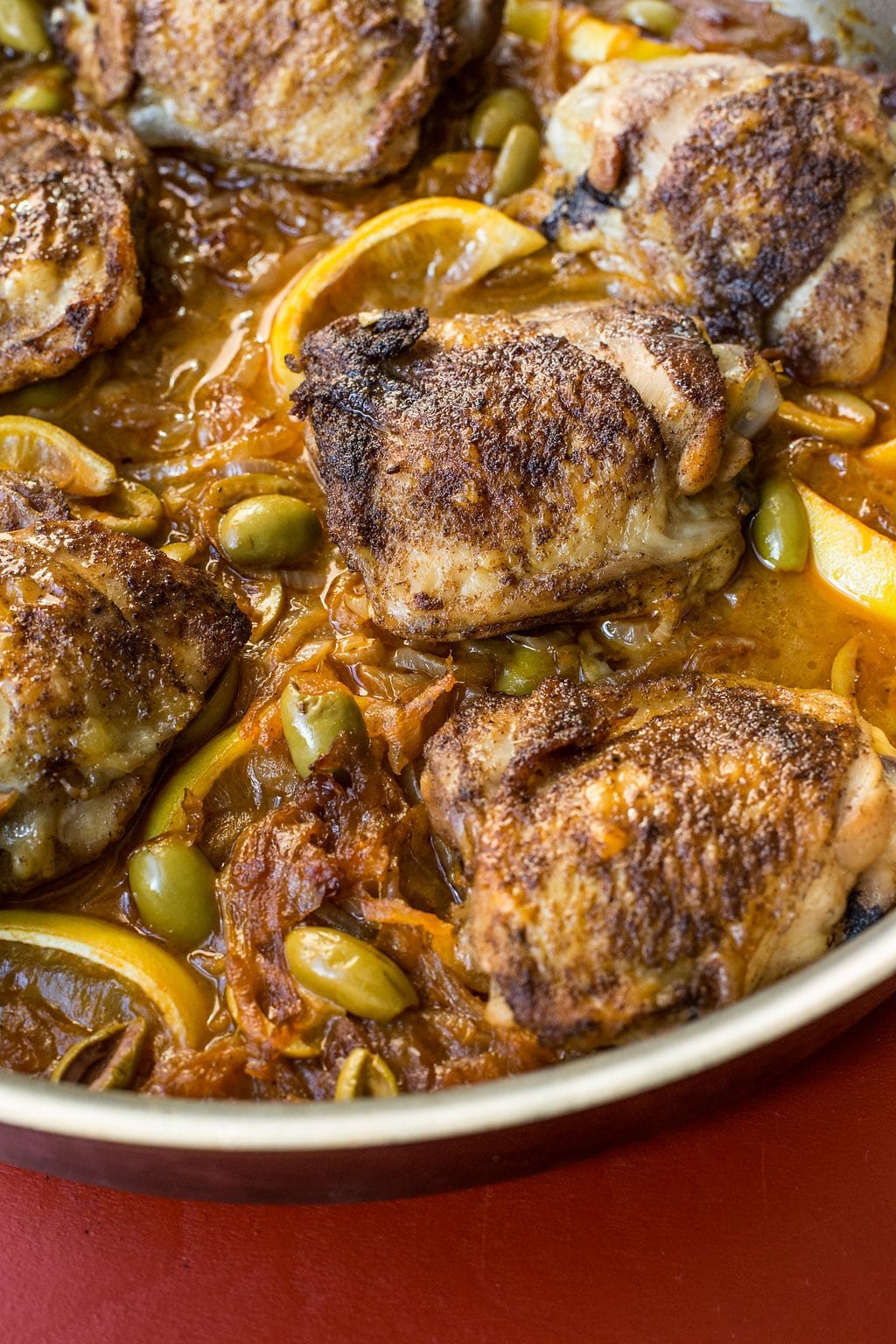 Chicken Thighs with Onions and Green Olives in a pan on a red surface.