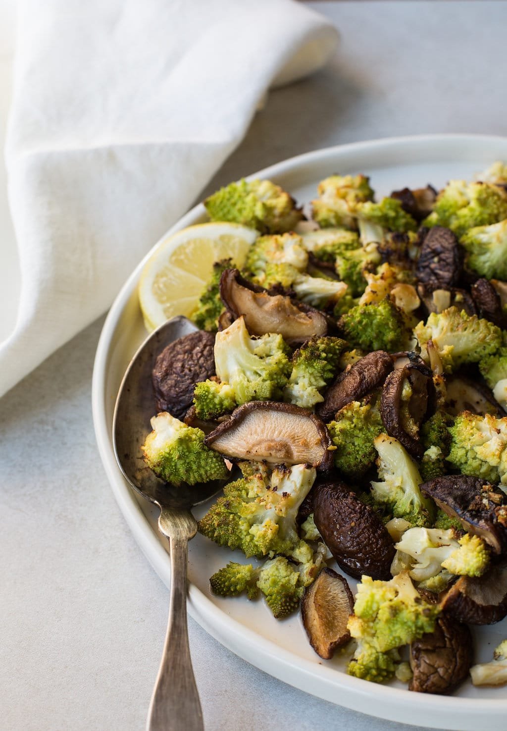 Roasted Broccoflower and Shiitake Mushrooms with Rosemary and Garlic in white bowl with spoon.