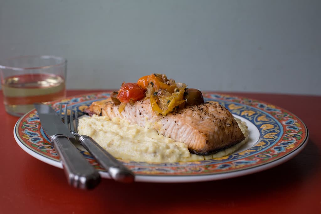 Silverware on a colorful plate with Salmon with Polenta and Warm Tomato Vinaigrette.