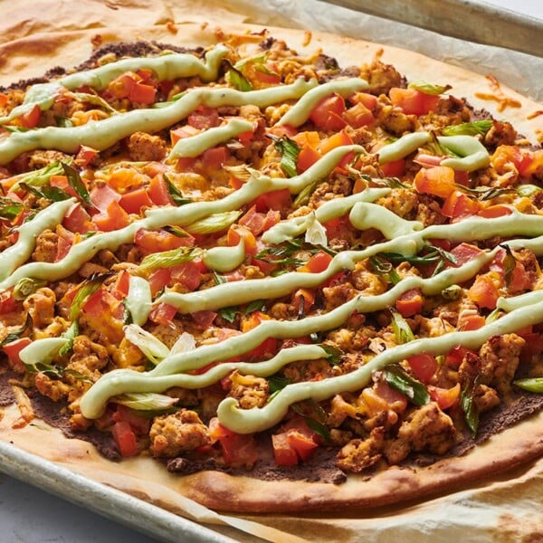 Mexican-inspired pizza with avocado crema on baking sheet.