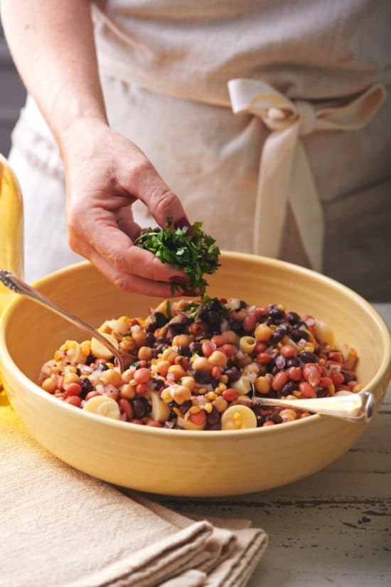 Woman topping a bowl of Modern Three Bean Salad with fresh herbs.