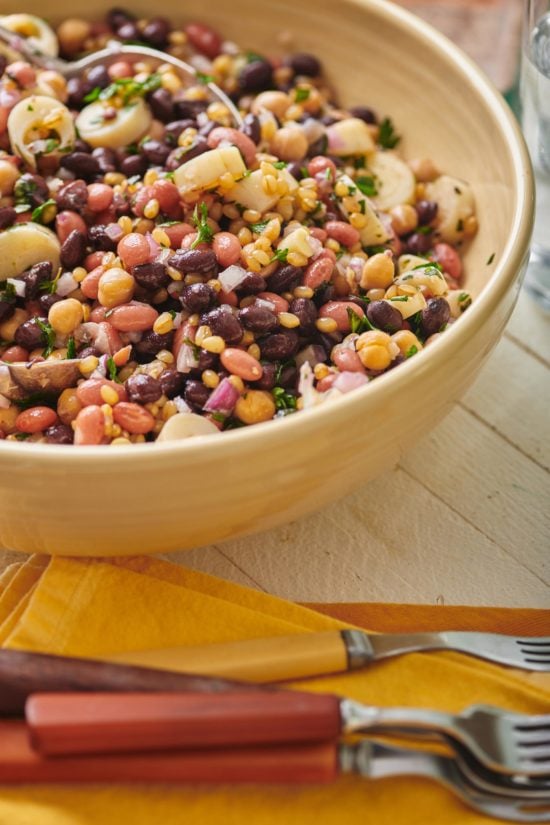 Light yellow bowl of Modern Three Bean Salad on a white, wooden table.