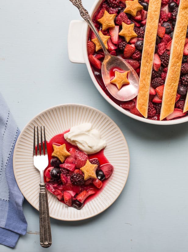 Small plate of Berry Cobbler with Whipped Cream next to a full dish.