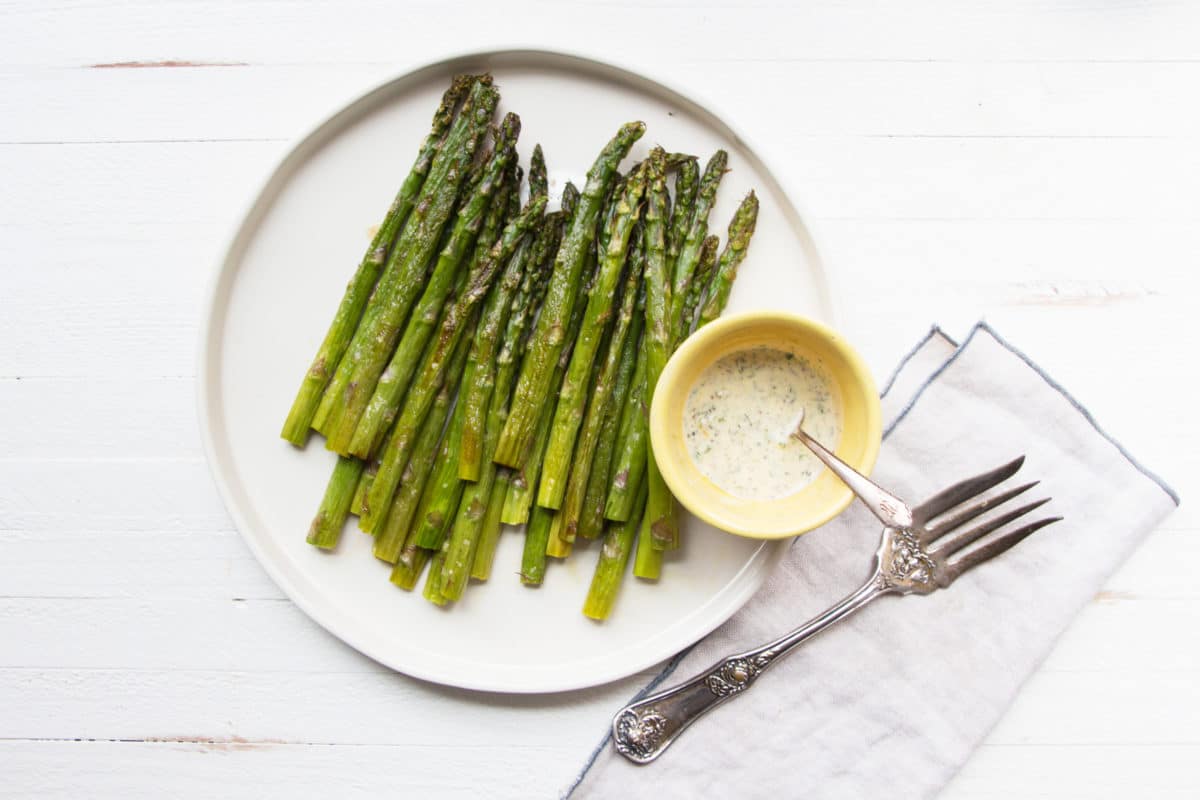 Roasted Asparagus on a plate with a bowl of Creamy Mustard-Oregano Sauce.